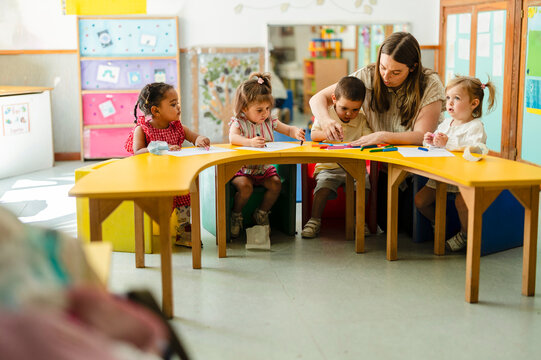 Teacher helping diverse children drawing in kindergarten classroom