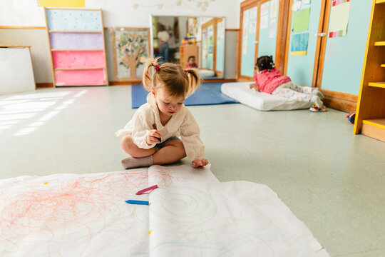 Little girl drawing on paper roll in classroom