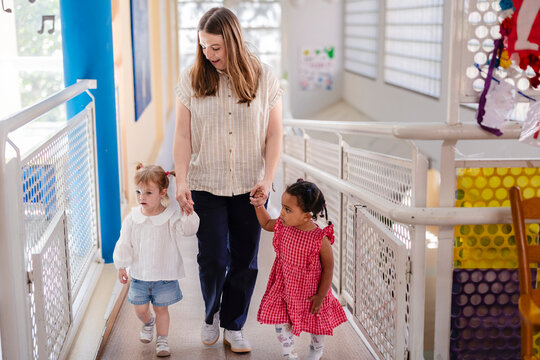 Woman guiding two diverse young girls walking in school hallway