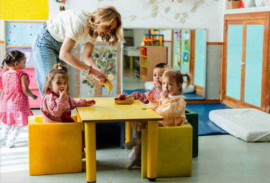Teacher helping happy children during healthy snack time
