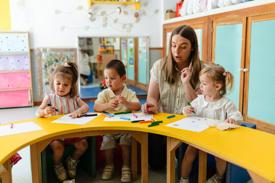 Teacher guiding preschool children drawing in classroom