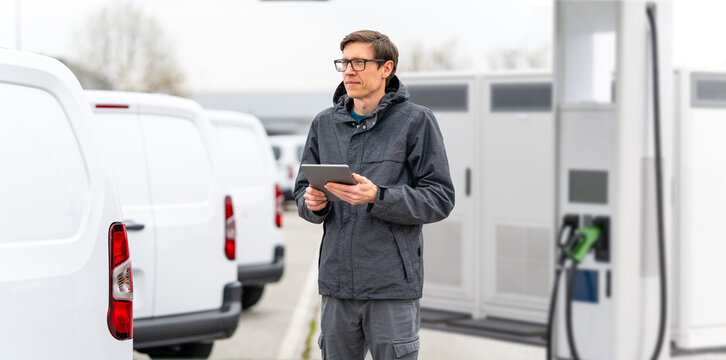 Fleet manager with digital tablet supervising rows of white electric delivery vans