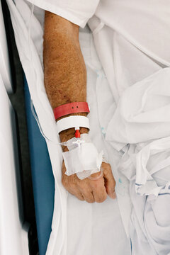 Patient&rsquo;s hand placed over hospital bedding with an intravenous line