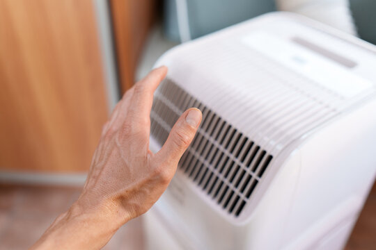 Man checking the freezing airflow from a running mobile AC unit during hot summer