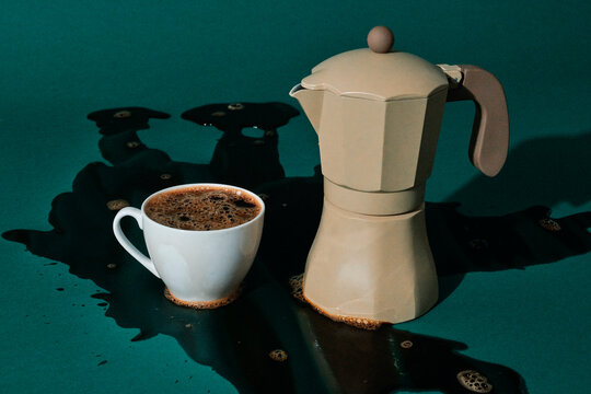 a cup and moka pot sit beside a wide coffee spill