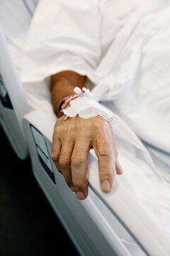 Close-up focuses on a patient's hand resting on white hospital sheets