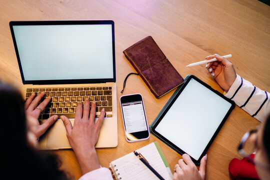 Two women are using a tablet and a laptop