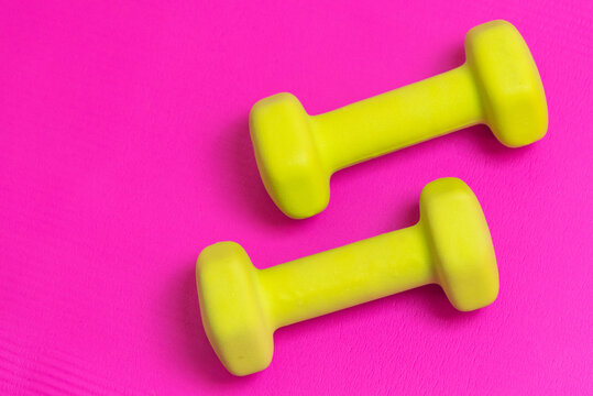 Two lime green dumbbells on a bright pink mat with space for copy on the left side