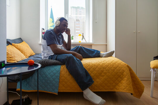 Young man listening to music with headphones on bed in dormitory