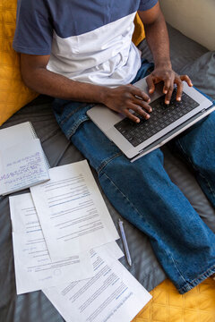 Student typing on laptop surrounded by study materials on bed
