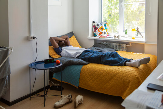 Person relaxing on bed in bright dormitory room