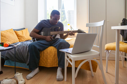 Student playing electric guitar during online lesson in dorm room