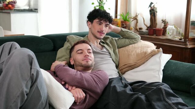 Romantic gay couple cuddling together on the couch while watching television in their apartment