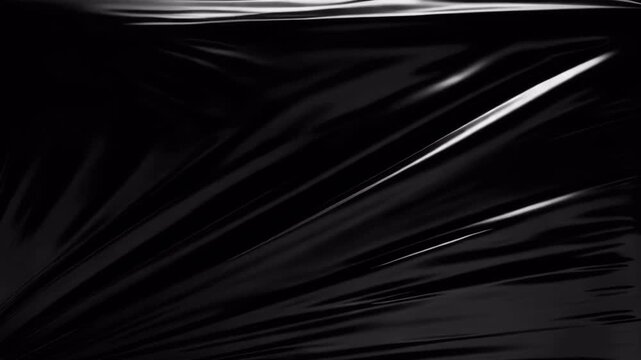 Abstract dark black plastic wrap texture with glossy light reflections.