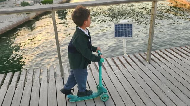 Young boy riding scooter by the water at sunset