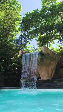 Waterfall cascades into clear pool surrounded by lush green trees