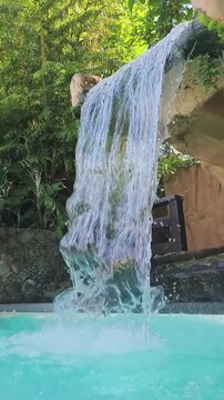 Water cascades down stone into clear blue pool surrounded by lush greenery