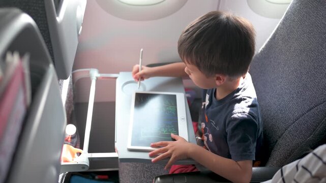 Young boy drawing on tablet in airplane seat with natural light