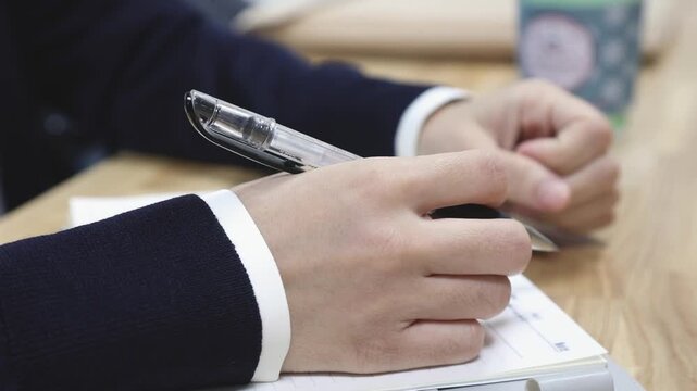 실내 사무실에서 회의나 업무 논의 중 펜을 잡고 노트에 내용을 메모하거나 기록하는 인물의 손동작을 가깝게 포착한 클로즈업 동영상 클립입니다.
