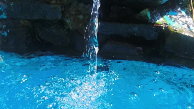 Water pours down into a bright blue pool surrounded by rocks