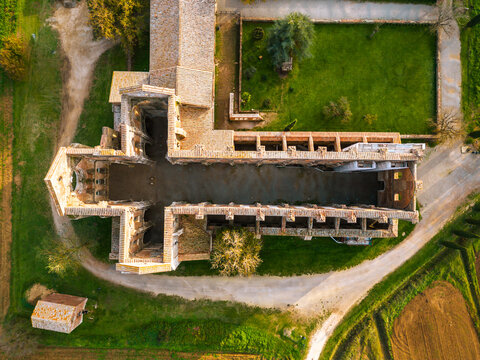 Aerial view of the roofless ruins of the historic Abbazia di San Galgano surrounded by green lawns and rural landscape in Chiusdino, Toscana, Italy.