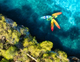 Aerial drone view of colorful kayaks in crystal clear turquoise sea near rocky coast and green trees. Summer outdoor adventure in Mallorca, Balearic Islands, Spain. Top down view of canoes. Travel © den-belitsky