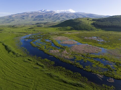 Lake on the edge of green hills, snow-capped mountains in the background under a clear blue sky, aerial view, landscape near Mirak, Mount Aragaz in the background, Aragatsotn province, Armenia