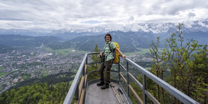 Mountaineer on a viewing platform, view over the village of Garmisch-Partenkirchen with cloudy mountains of the Wetterstein range, Ammergau Alps, Bavaria, Germany