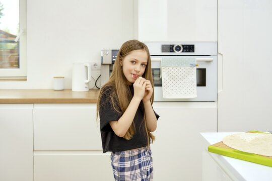 Young funny girl bites a piece of fresh flatbread in the kitchen