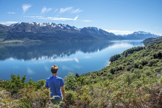 Young man looking over Lake Wakatipu, mountains reflected in the lake, Otago, South Island, New Zealand