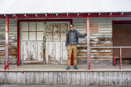 Young man standing on the porch of a former Gold Mine Independence Mine building in mountainous landscape, Independence Mine State Historical Park, Hatcher Pass, Talkeetna Mountains, Alaska, USA
