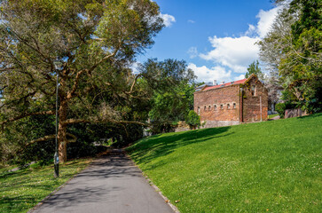 Naklejka premium Paved pathway beside grassy hill with historic brick building in Albert Park, Auckland, New Zealand, 1 January 2024