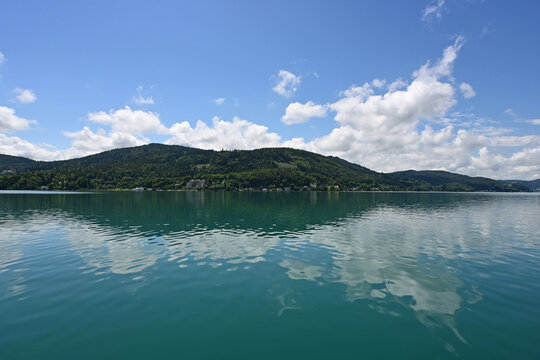 View of placid Lake Worthersee near Klagenfurt, Austria with summer cloudscape reflected in calm water.