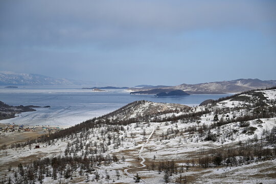 Beautiful view of the coast of the Small Sea of Lake Baikal, Kurkut Bay, tourist camps and wooden hotel houses. Winter landscape