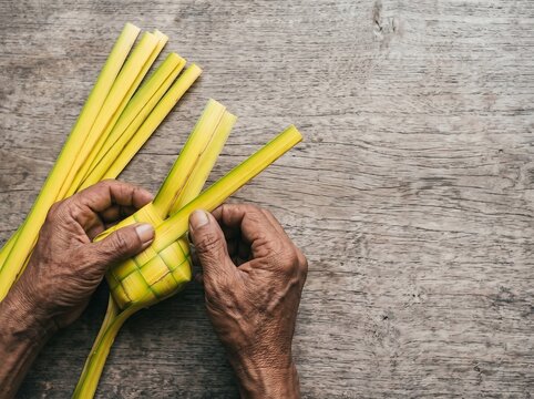 Senior hands weaving a traditional Ketupat from yellow palm leaves