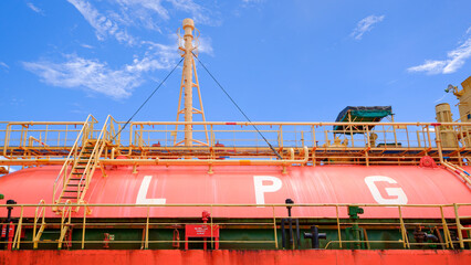 Naklejka premium Large LPG storage tank on a cargo ship vessel under blue sky. Liquefied petroleum gas transportation and maritime energy logistics industry