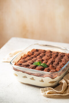 Traditional Italian dessert tiramisu in a glass backing form on light background