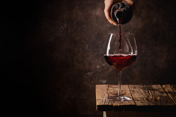 Fototapeta premium Pouring red wine into the glass against rustic dark wooden background