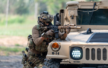 Fototapeta premium One army man point gun to enemy direction and lean on front hood of High Mobility Multipurpose Wheeled Vehicle to practice of fight with enemy.