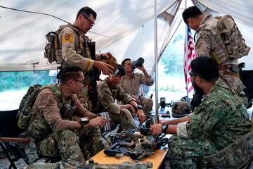 Fototapeta premium Close up shot group of army with different types of equipment and weapons have meeting and plan inside field tent.