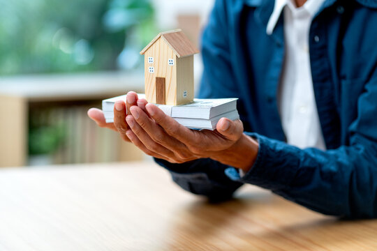 Close up man hands hold stack of money and house model in concept of collect income for home payment in the future.