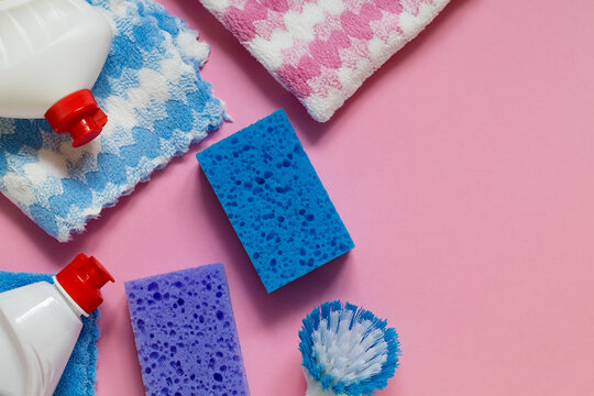 Cleaning essentials arranged in a flat lay composition with vibrant sponges, reusable cloths, and detergent bottles on pink. Copy space.