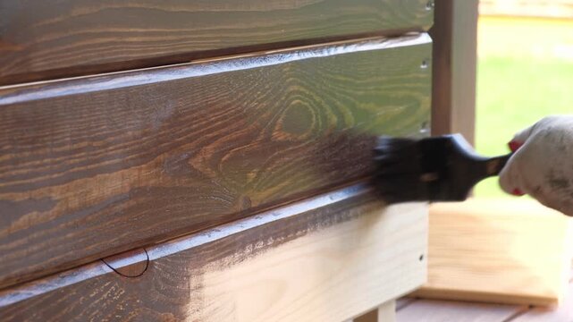 Brown oil for protection of wood by staining. Painting fence for protecting and pests. Woodworker applying finish to pine board box. Repairman varnishing with brush wooden fencing wall plank surface.