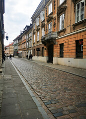 Fototapeta premium Warsaw poland quiet street with historic buildings and textured pavement in old town area. Scene represents travel, heritage, urban life, and architectural detail concept.