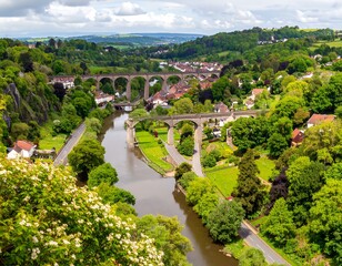 Obraz premium A scenic vista showcasing a winding river, flanked by verdant trees, historic stone viaducts, and charming buildings
