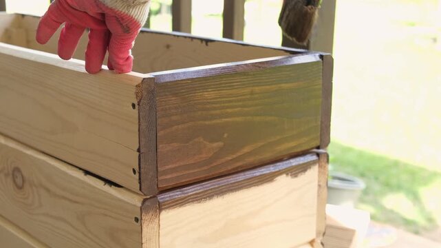 Brown oil for protection of wood by staining. Painting fence for protecting and pests. Woodworker applying finish to pine board box. Repairman varnishing with brush wooden fencing wall plank surface.
