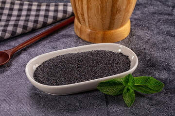 Poppy seeds in white bowl with fresh mint leaf garnish. Culinary ingredient on dark textured background © Andrei Starostin
