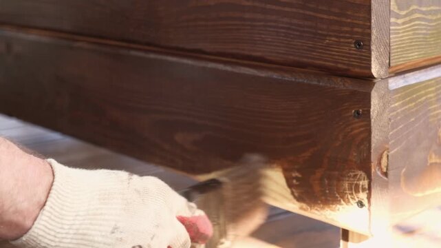 Brown oil for protection of wood by staining. Painting fence for protecting and pests. Woodworker applying finish to pine board box. Repairman varnishing with brush wooden fencing wall plank surface.