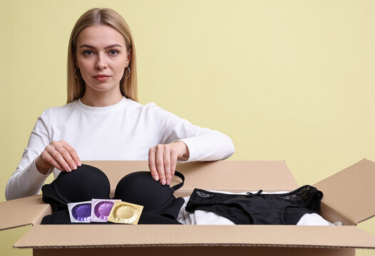 Woman packing cardboard box with black underwear brassiere and condoms