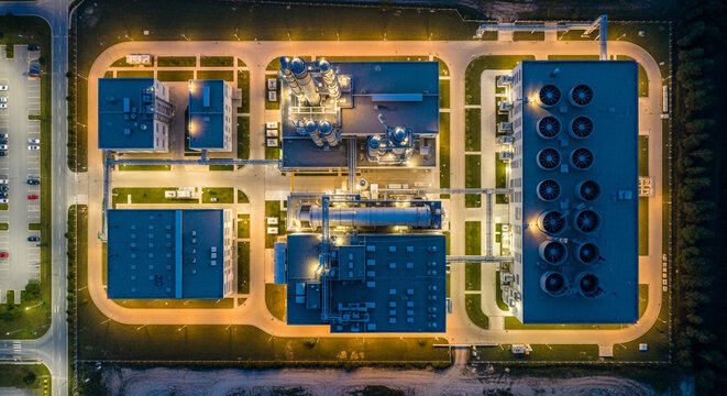 Aerial view of an illuminated industrial facility at night featuring cooling fans and complex infrastructure
